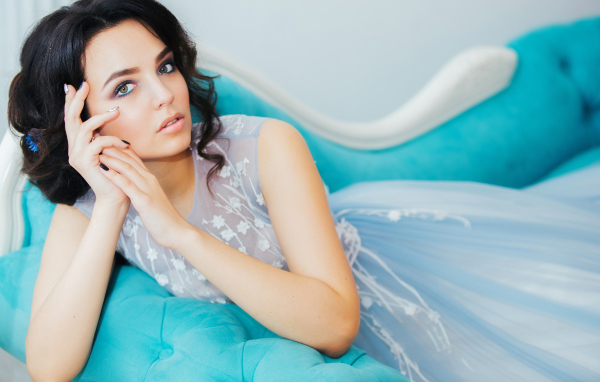 Девушка брюнетка в красивом платье лежит на голубом диване