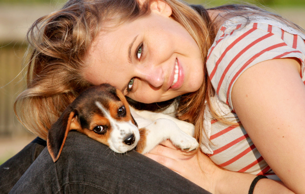 Убающаяся девушка шатенка с милым щенком на руках