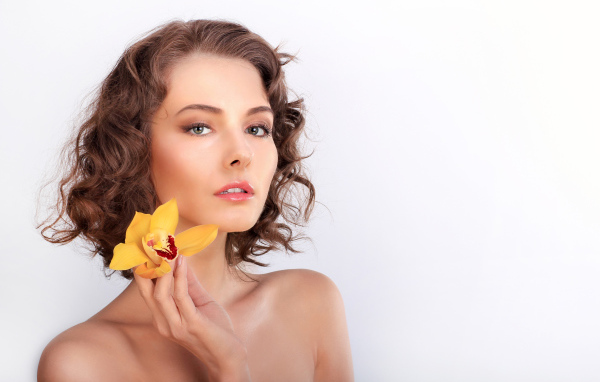 Нежная девушка шатенка с желтым цветком орхидеи в руке