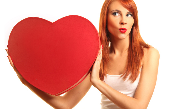 Рыжеволосая девушка с большим красным сердцем в руках на белом фоне