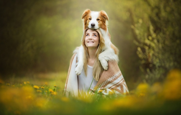 Улыбающаяся девушка с собакой сидят на траве
