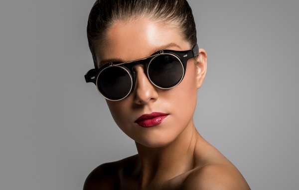 Лицо девушки в черных очках на сером фоне