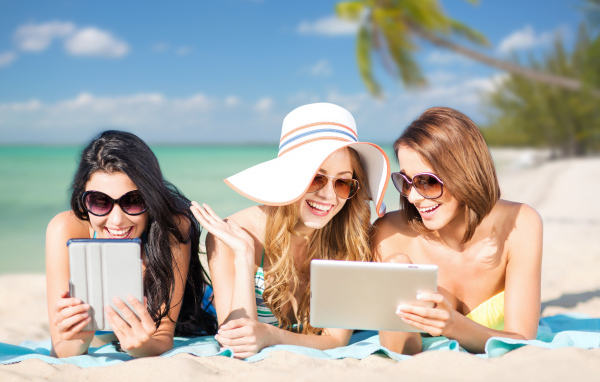 Три улыбающиеся девушки загорают на пляже с планшетами в руках