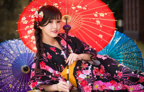Молодая азиатка в кимоно с разноцветными зонтиками