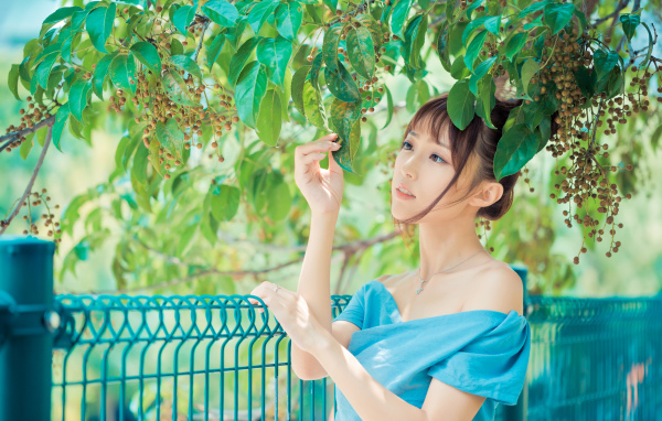 Молодая красивая девушка азиатка стоит у ветки с зелеными листьями