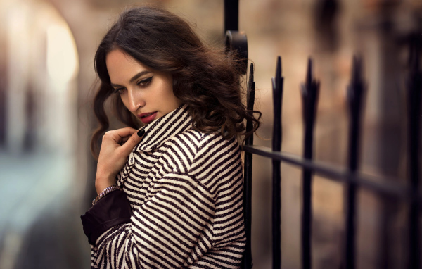 Молодая брюнетка в пальто у забора