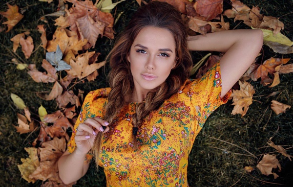 Молодая брюнетка лежит на траве с сухими листьями
