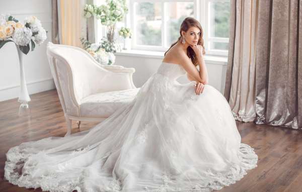 Молодая девушка в красивом свадебном платье сидит в белом кресле
