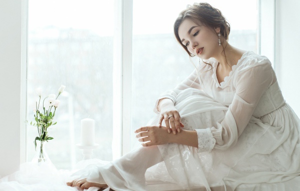 Молодая грустная девушка в белом платье у окна