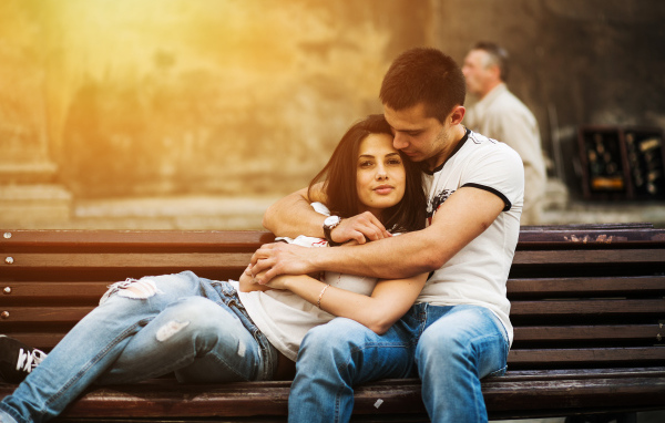 Влюбленная пара сидит на деревянной лавке в парке