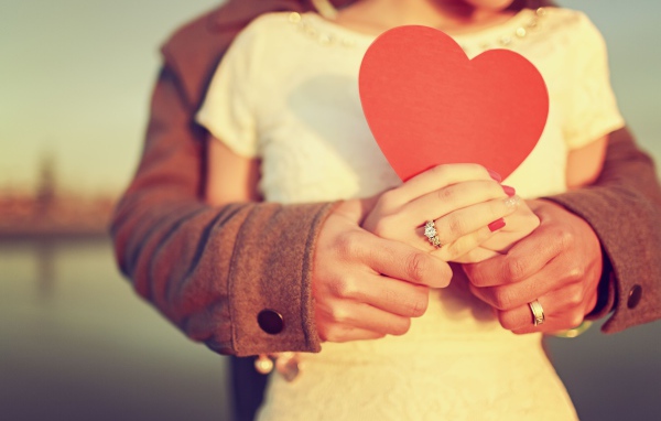 Влюбленная пара держит в руках красное бумажное сердце