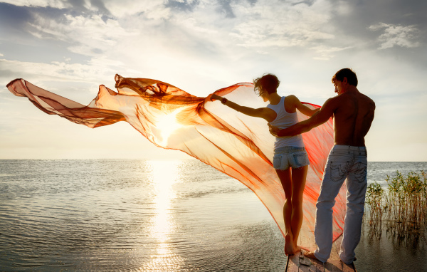 Молодая влюбленная пара гуляет у моря на закате