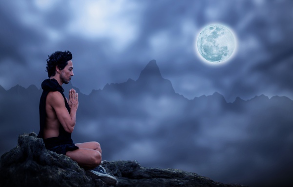 Мужчина медитирует на камне ночью в полнолуние