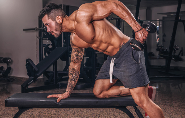 Мускулистый мужчина занимается в спортзале с гантелей