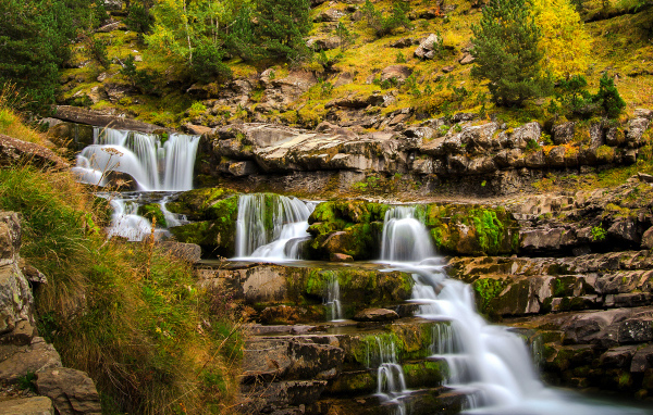 Быстрый ручей стекает по скале в осеннем лесу