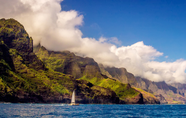 Парусная лодка плывет по голубой воде на фоне покрытых зеленью гор