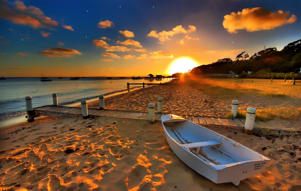 Белая лодка на пляже под закатным солнцем