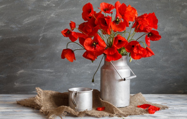 Букет красных маков в железном бидоне на столе с кружкой