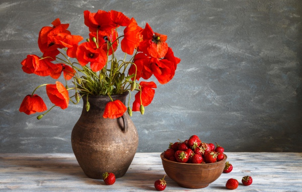 Красивый букет красных полевых маков в вазе на столе с клубникой