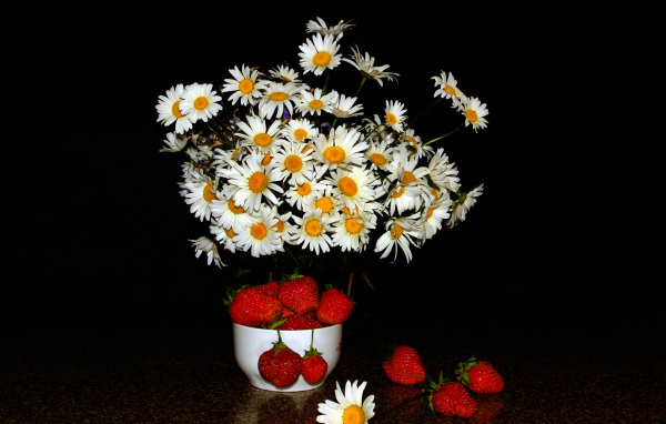 Белые полевые ромашки и клубника на столе на черном фоне