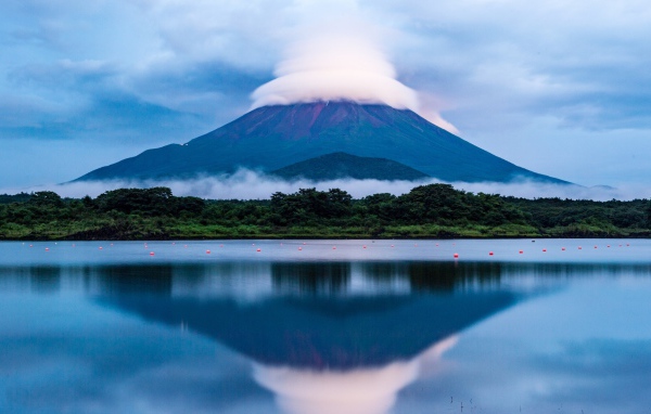 Вулкан Фудзияма в белых облаках отражается в воде озера