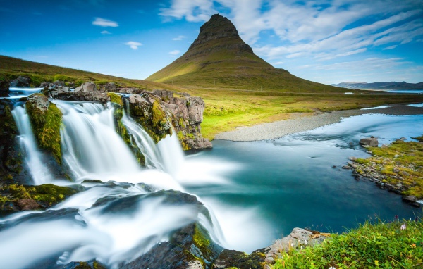 Водопад стекает в реку на фоне горы под красивым небом