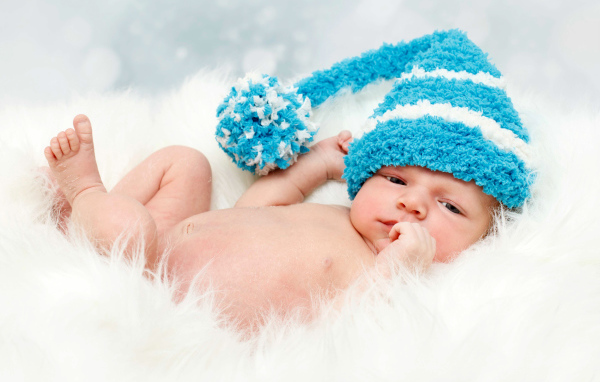 Грудной ребенок в голубой шапке с бубоном на голове