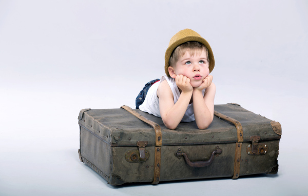 Маленький мальчик лежит на большом чемодане на сером фоне