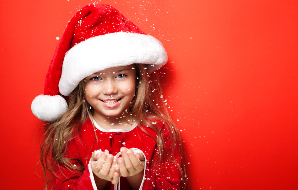 Маленькая девочка в новогодней шапке ловит руками снежинки