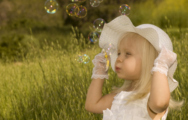 Маленькая девочка в большой белой шляпе пускает мыльные пузыри