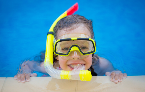 Маленькая девочка в маске с трубкой плавает в бассейне