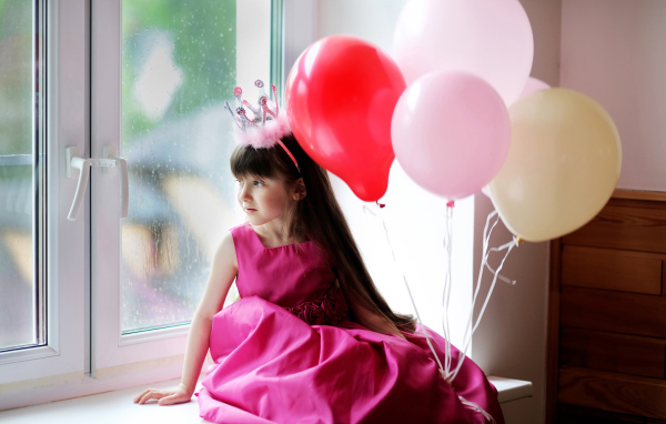 Маленькая девочка в костюме принцессы сидит на окне