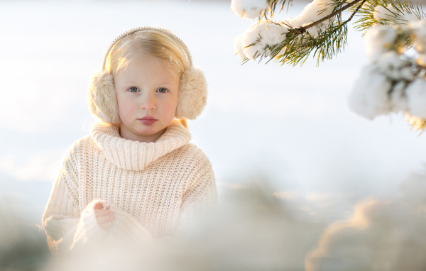 Маленькая девочка в белом свитере у покрытой снегом ели