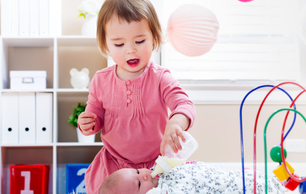 Маленькая девочка кормит из бутылочки маленького брата