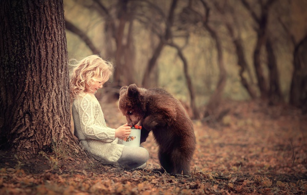 Маленькая девочка сидит у дерева с медвежонком гризли