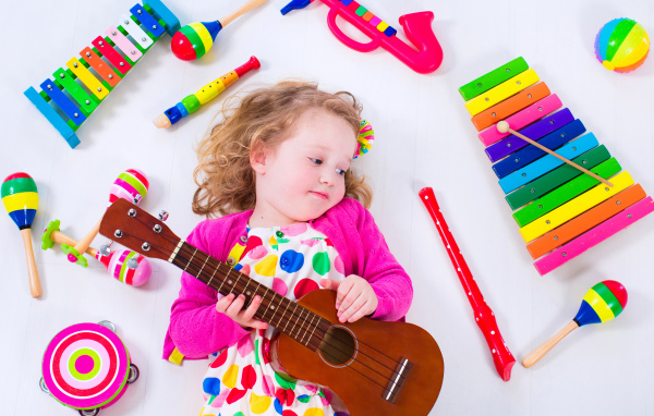 Маленькая девочка с гитарой лежит рядом с детскими музыкальными инструментами