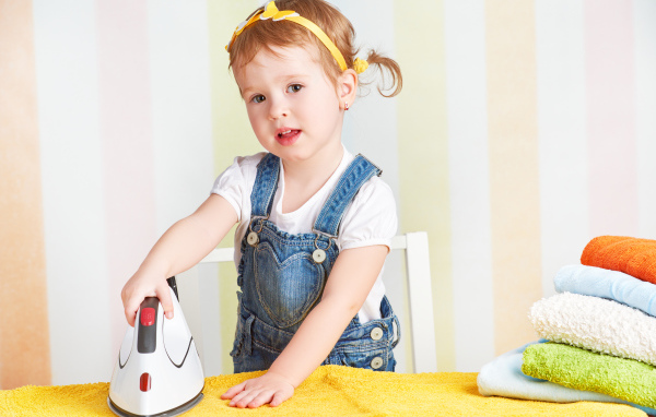 Маленькая девочка с утюгом гладит полотенце