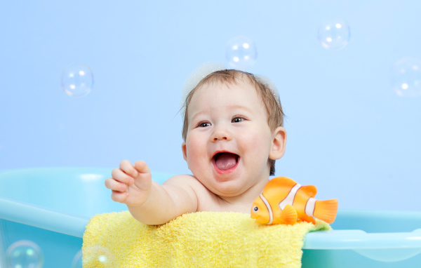 Веселый малыш купается в ванной с игрушечной рыбкой