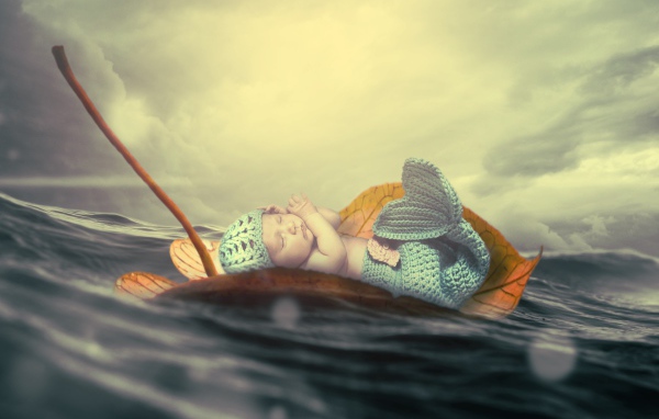 Маленький грудной ребенок в костюме русалки плывет на листе в океане