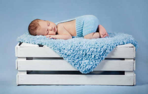Маленький грудной ребенок спит на синем покрывале на деревянном ящике