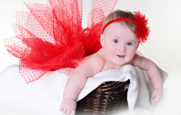 Маленькая голубоглазая девочка в красном красивом платье лежит в корзине