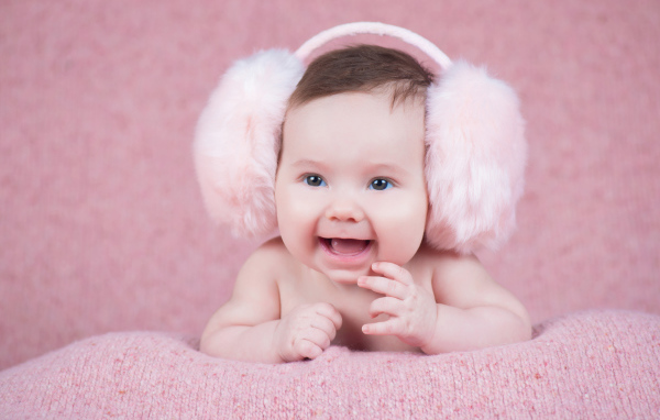 Милый улыбающийся младенец в больших розовых наушниках