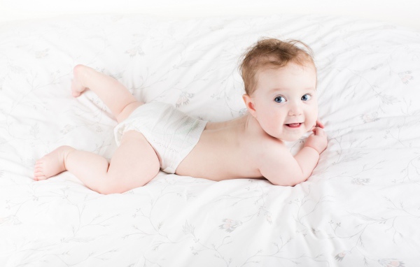 Забавный голубоглазый малыш лежит на белом покрывале