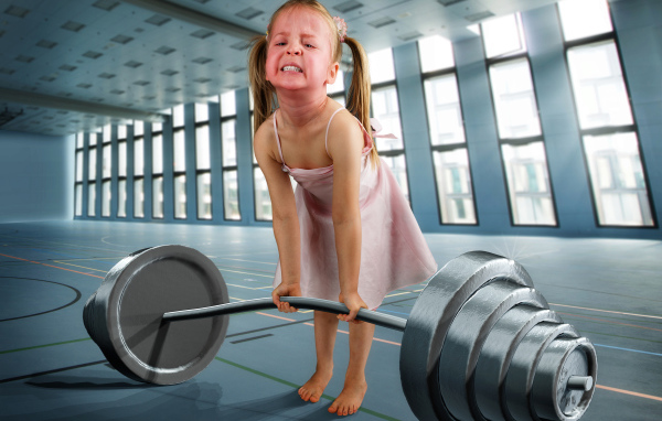 Смешная девочка пытается поднять тяжелую штангу