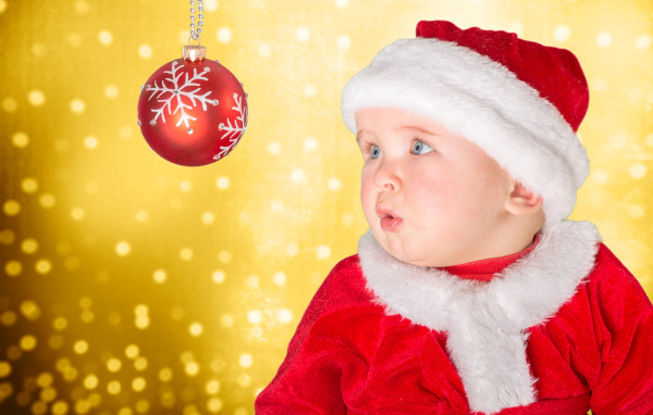 Маленький грудной ребенок в костюме Санты смотрит на елочный шар