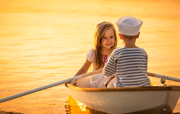 Маленькие мальчик и девочка плывут в лодке на закате солнца