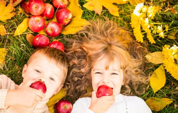 Маленькие мальчик и девочка лежат на желтой листве с красными яблоками