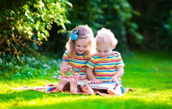 Маленькие мальчик и девочка читают книгу сидя на зеленой траве