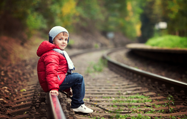 Маленький мальчик в красной куртке сидит на рельсах