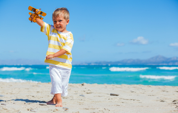 Маленький мальчик на пляже с игрушечным самолетом в руках